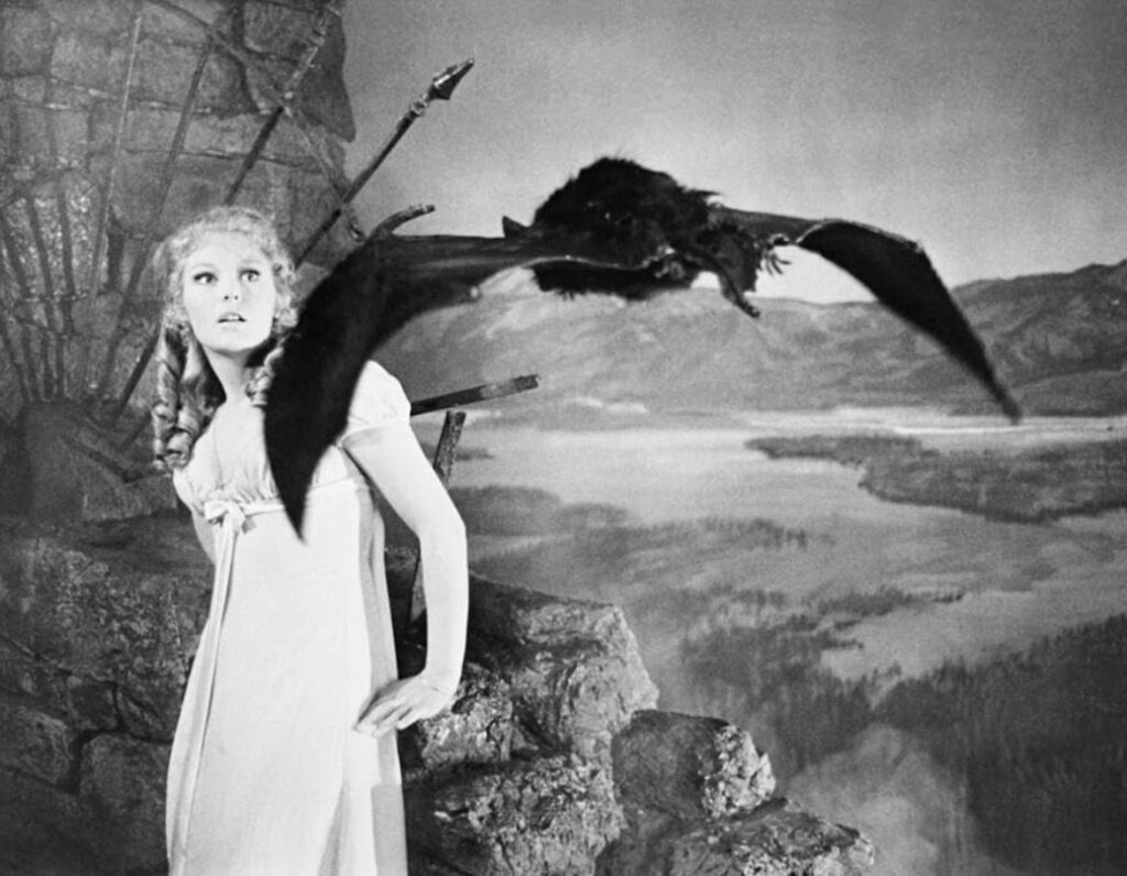 A young woman in a nightgown looks frightened as a huge bat puppet swoops towards her.